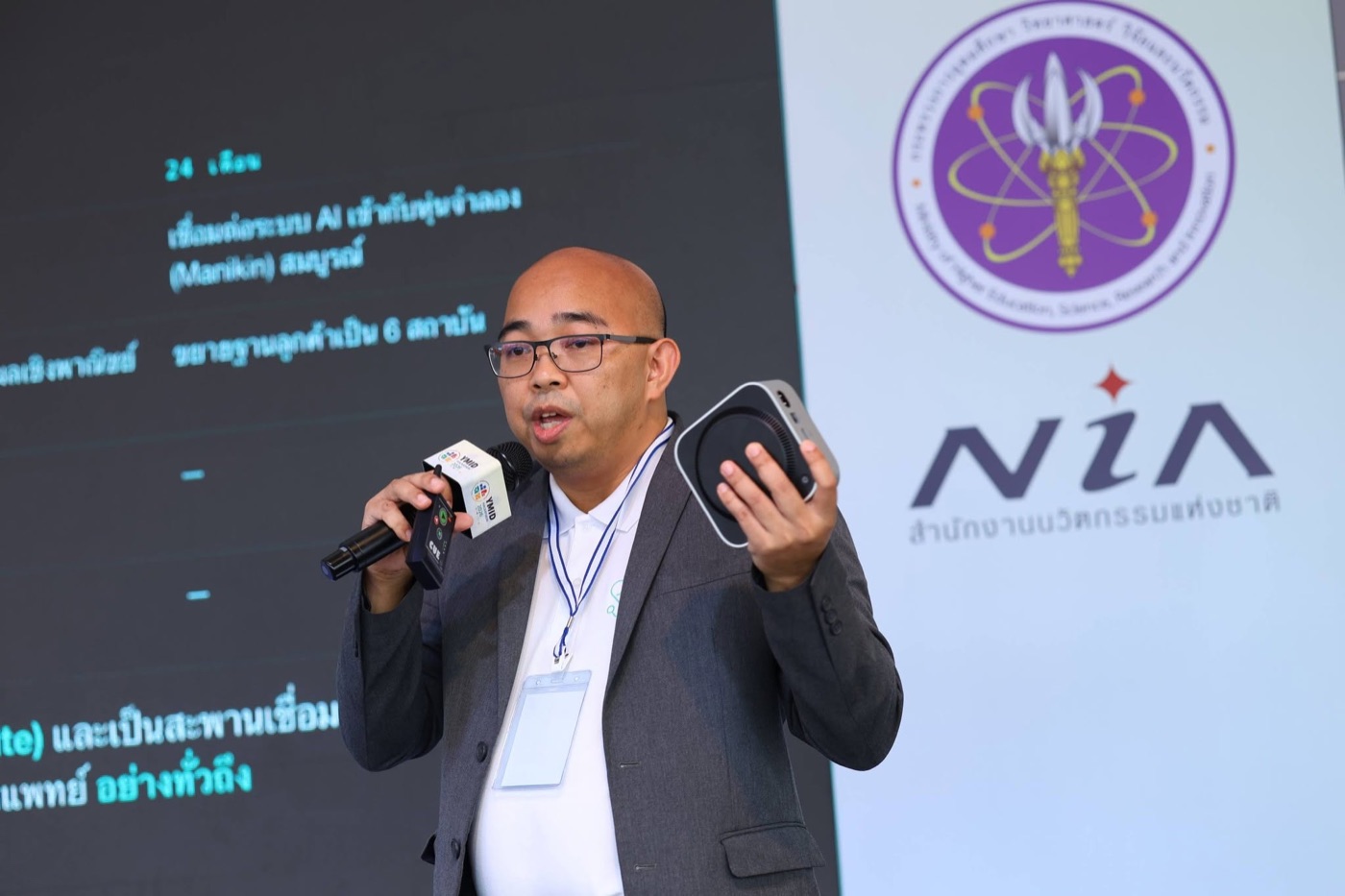 ผู้ก่อตั้ง MEGA WIZ นำเสนอ Embla Box บนเวที YMID Hackathon 2026 ฉากหลังโลโก้ NIA